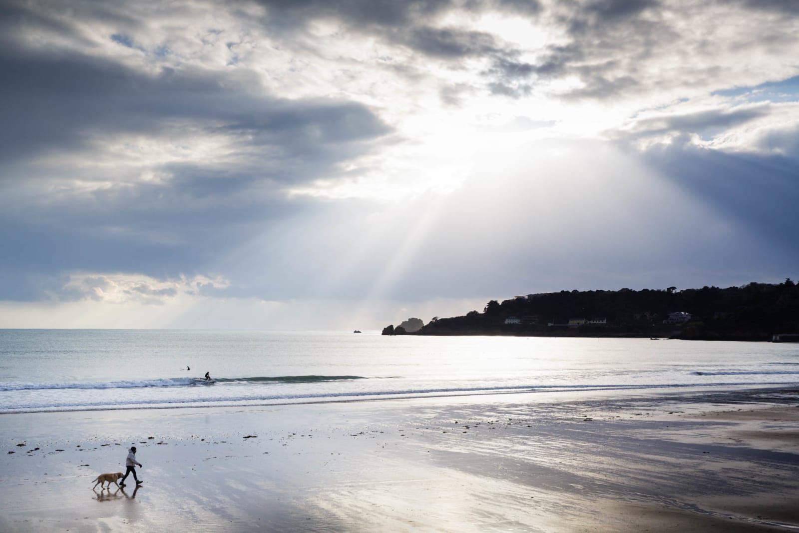 St Brelades Bay channel island of Jersey sunset sunrise dawn stunning  vibrant orange sky beautiful seashore sand beach in morning and evening  hotel clouds horizon reflecting sun on ocean tractor boat Stock