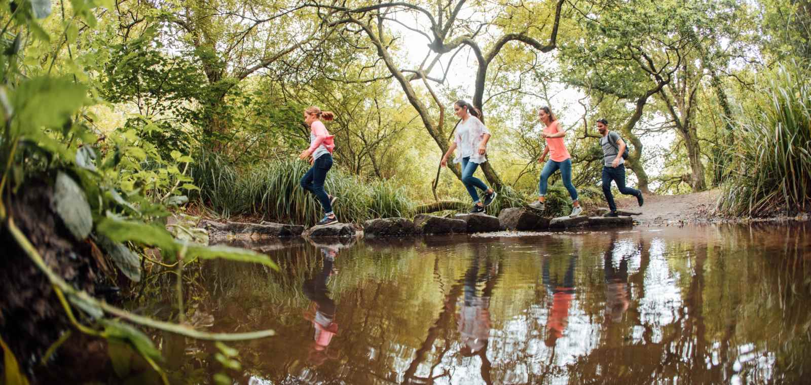 Family hoping over stepping stones in a stream at St. Catherine's Woods