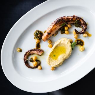 Octopus dish on a white plate with hummus