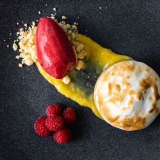 Meringue-topped dessert with raspberries, lemon curd, and raspberry sorbet arranged artistically on a black plate