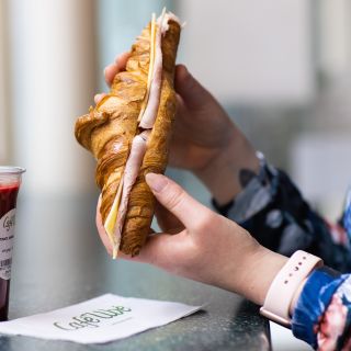 A fresh croissant filled with ham and cheese, accompanied by a purple beetroot drink