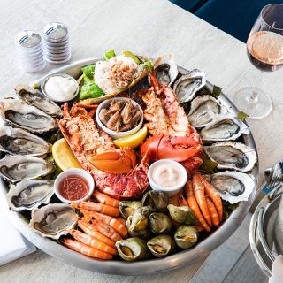 A seafood platter of lobster, cockles, oysters, prawn and scallops, accompanied by a bottle of rosu00e9 wine