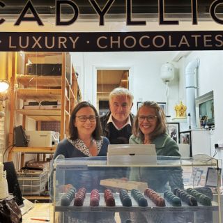 Looking into the window of the Chocadyllic Studio Shop with Evelyn Day and 2 guests and chocolates and Corbiere lighthouse in chocolate sculpture