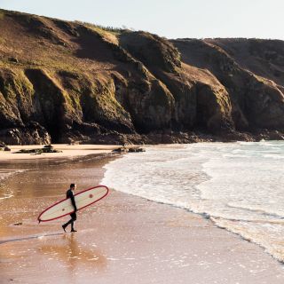 Surfer walking to the sea at Plu00e9mont Bay