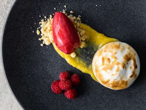 Meringue-topped dessert with raspberries, lemon curd, and raspberry sorbet arranged artistically on a black plate