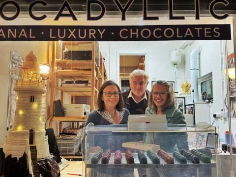 Looking into the window of the Chocadyllic Studio Shop with Evelyn Day and 2 guests and chocolates and Corbiere lighthouse in chocolate sculpture