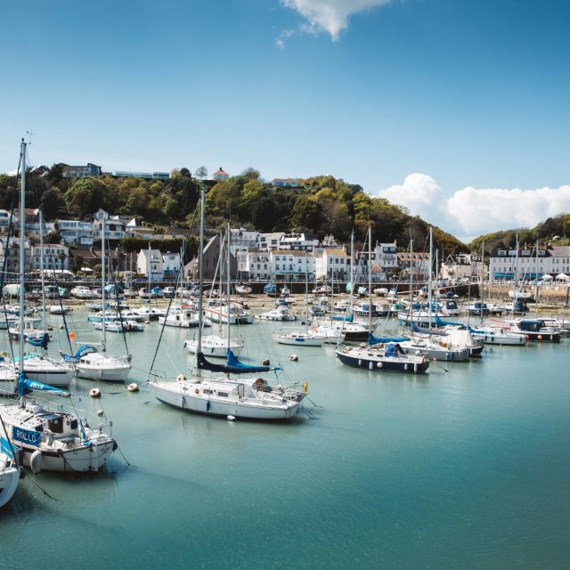 several small sailing boats moored in the marina in front of the village of St Aubin, Jersey, on a bright clear day