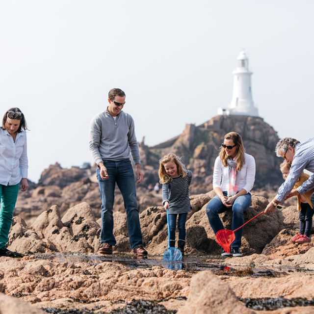 Family rock pooling on beach in front of corbiere lighthouse