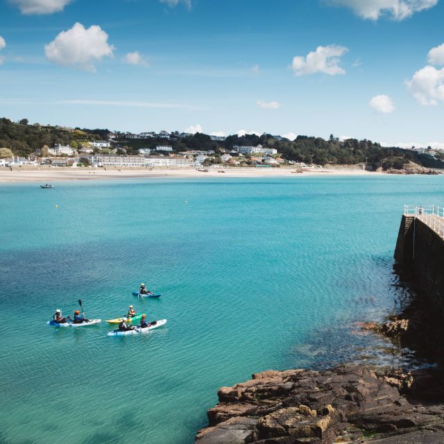 Kayakers paddle next to the pier in St. Brelade