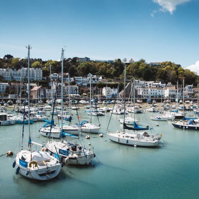 several small sailing boats moored in the marina in front of the village of St Aubin, Jersey, on a bright clear day