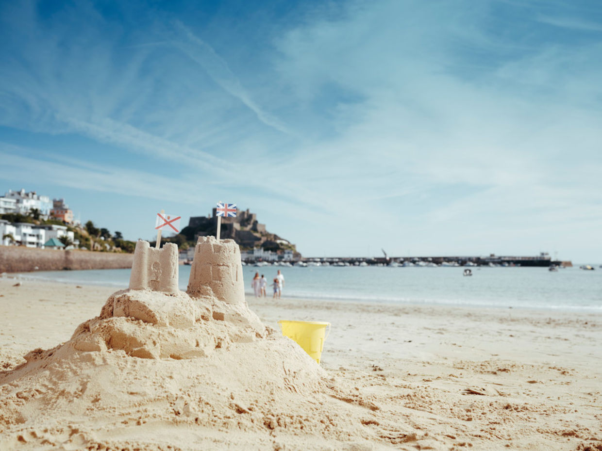 Sand castle on white sandy beach with sea and castle as a back drop