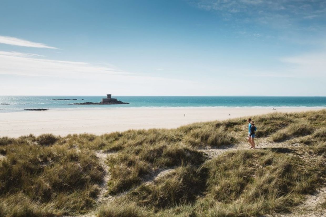 View over sand dunes and St Ouens beach with La Rocco Tower in background