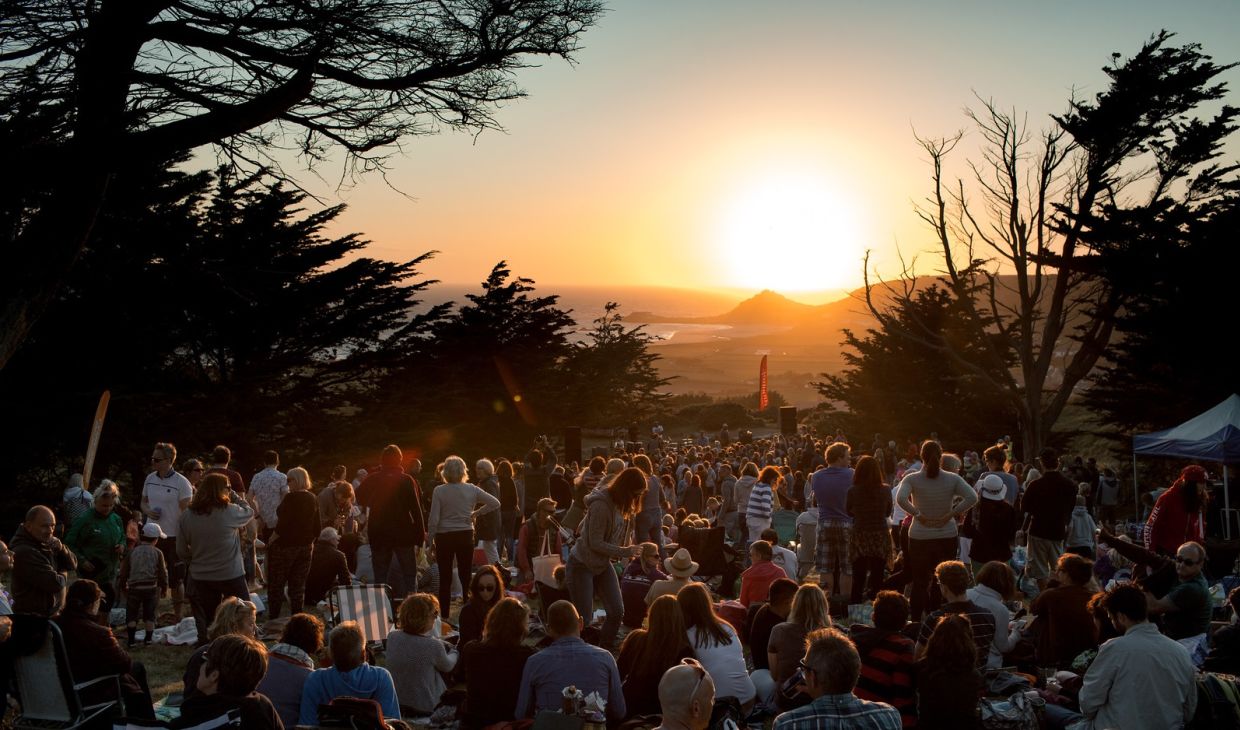 The sun sets over a crowd enjoying a outdoors concert