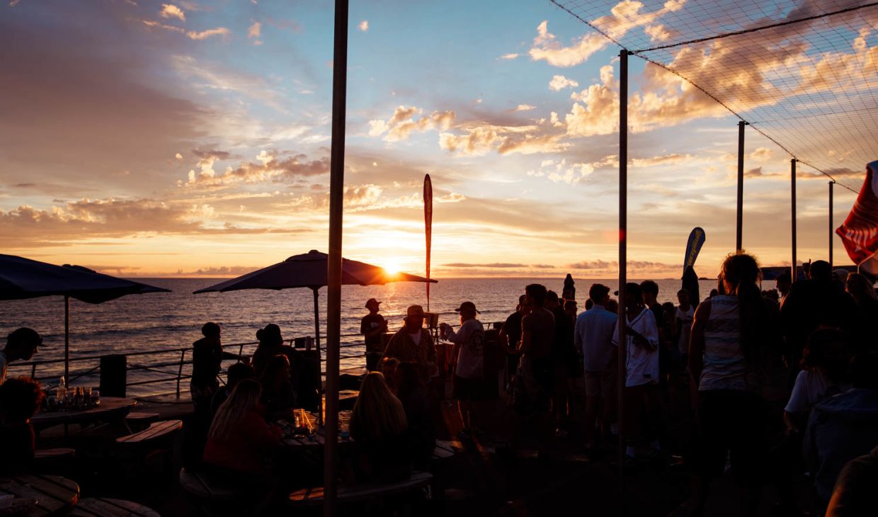 People at a bar by the sea at sunset