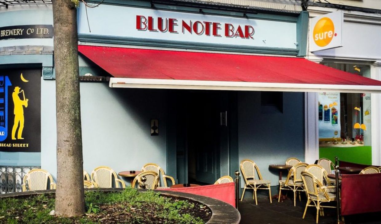 A picture of the exterior of the blue note bar in jersey. There is a patio area for drinking.
