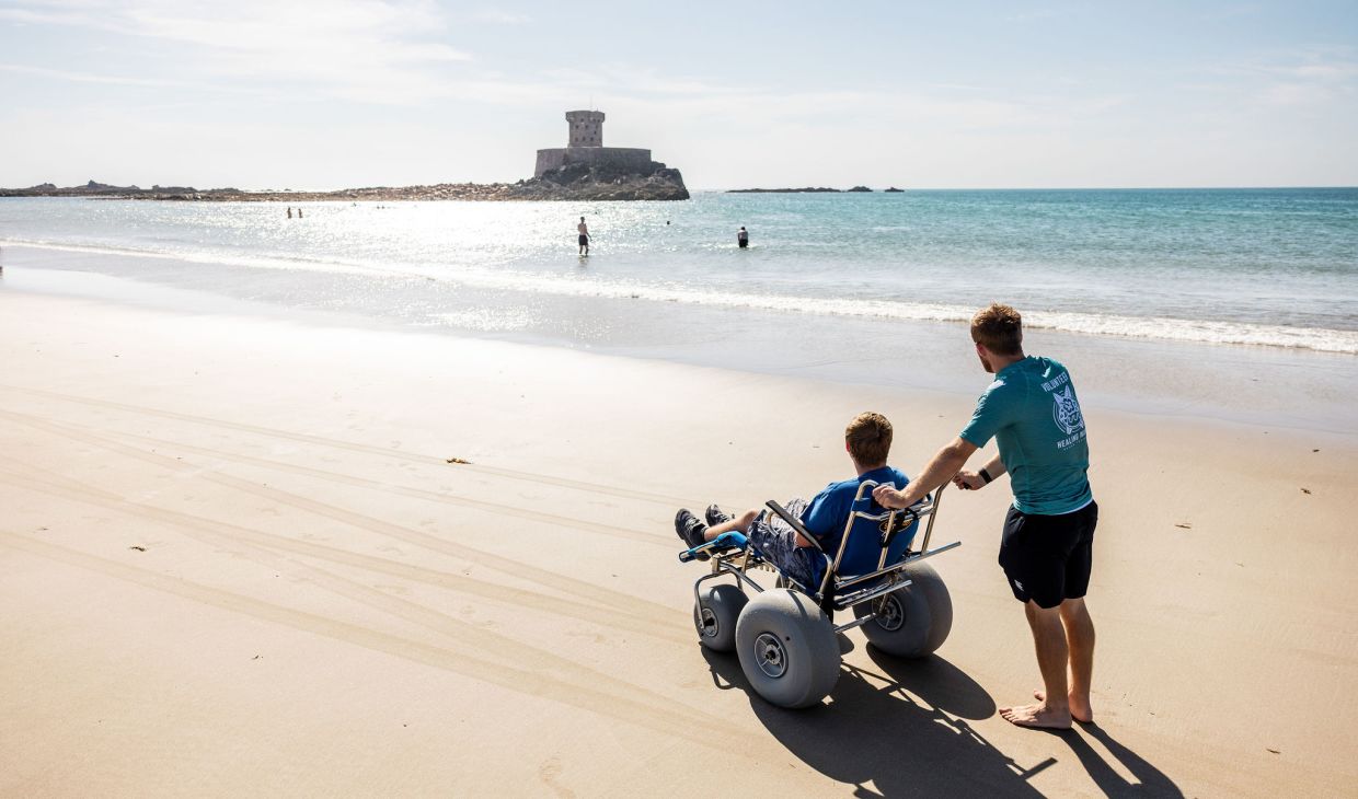 Person pushing a wheelchair user across the sand