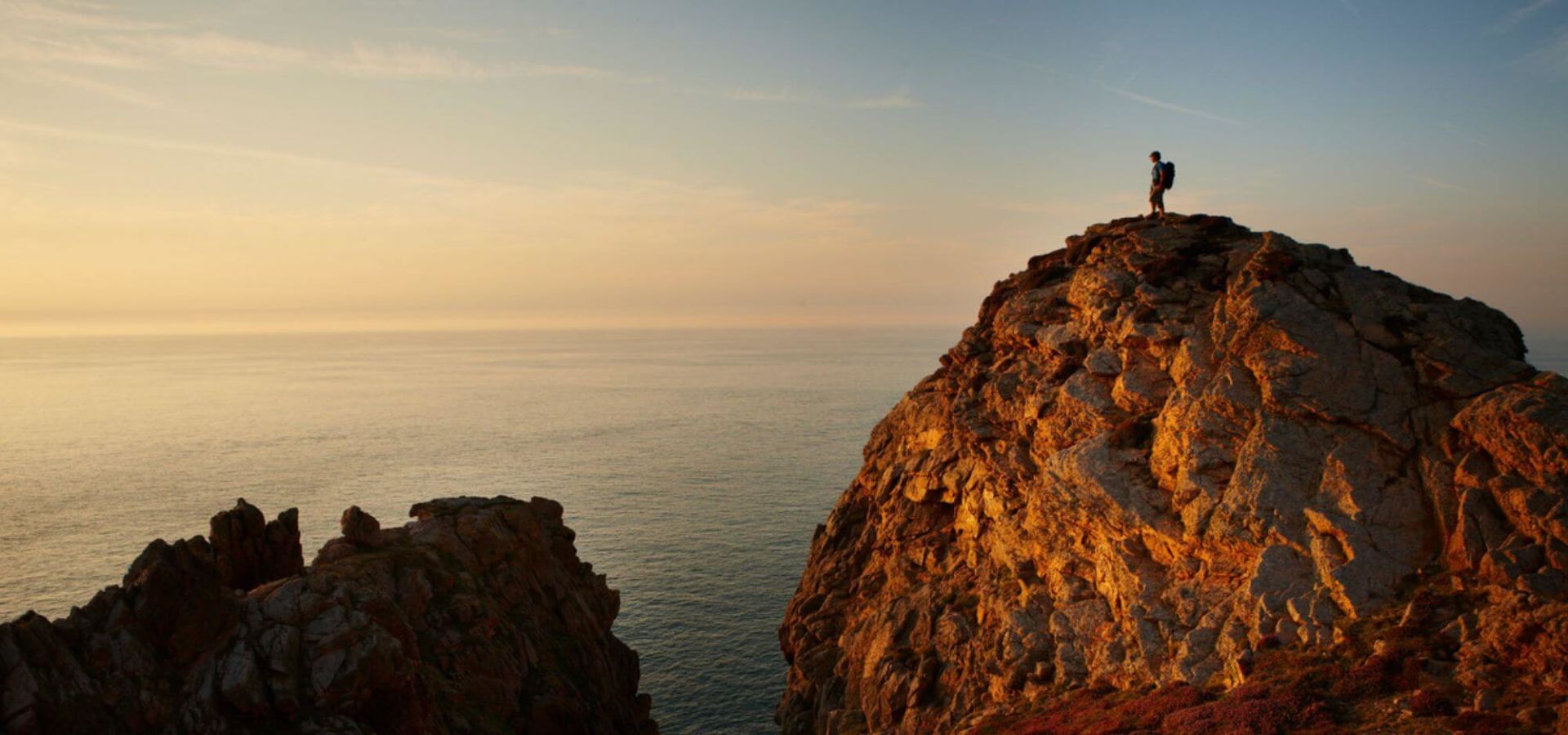 Person standing on cliff in distance at sunset