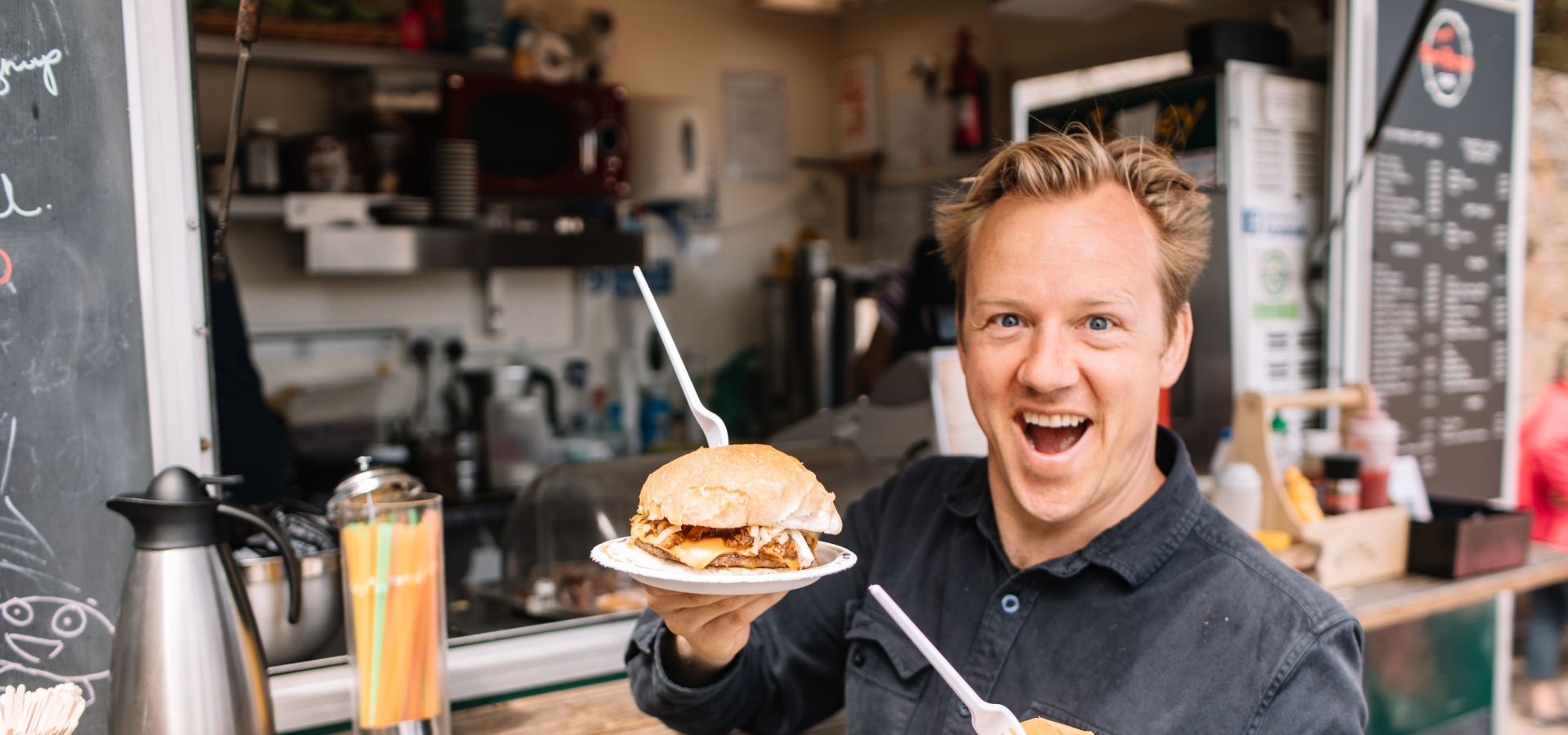 A man at a beach kiosk looking very happy holding two breakfast rolls