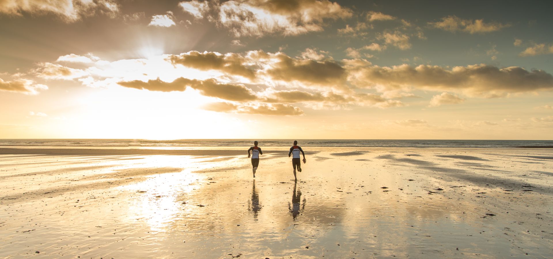 Two people running on the beach towards the sea at sunset