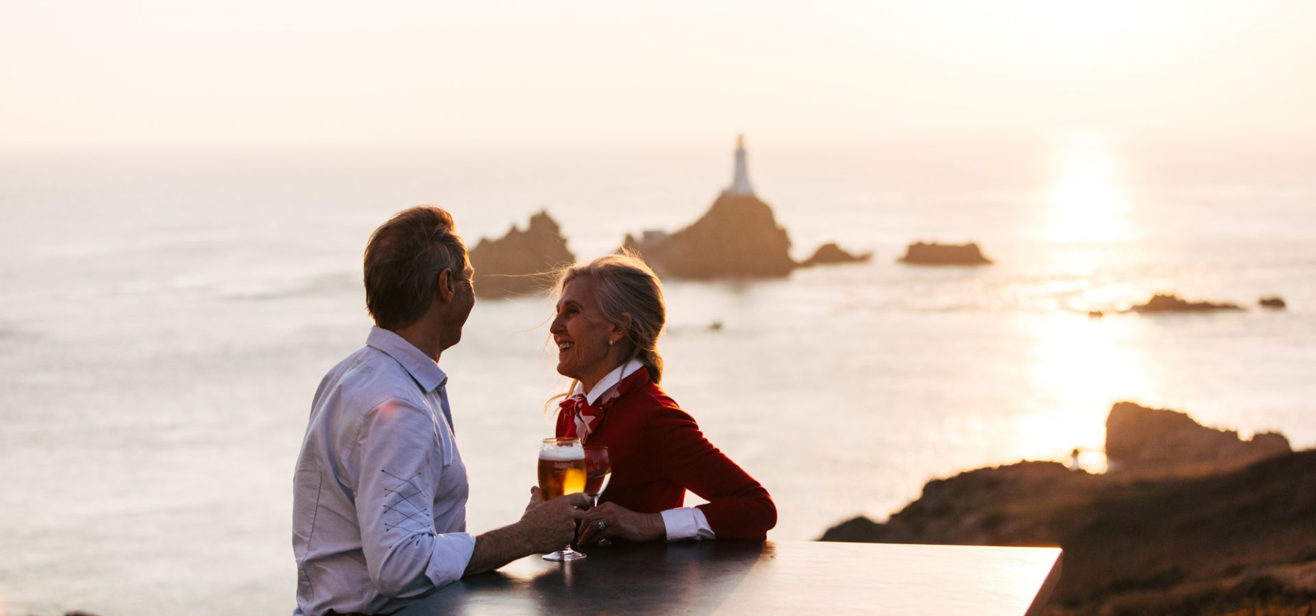 A couple having a drink with La Corbière Lighthouse in the background