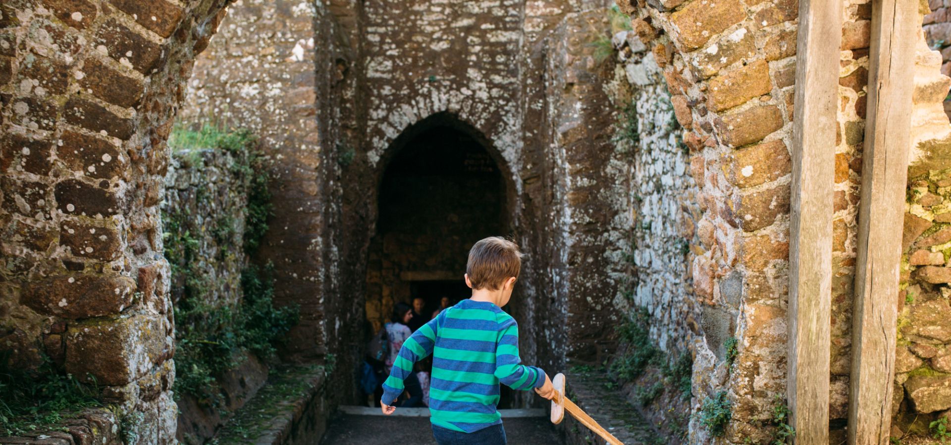 A child running through Mont Orgueil Castle with a wooden sword