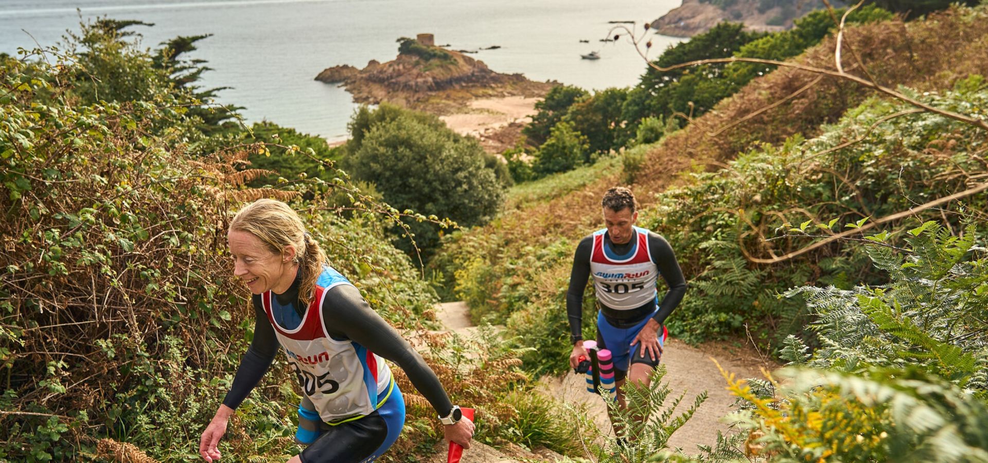 Man and a woman running on a coastal path wearing sportswear in Jersey