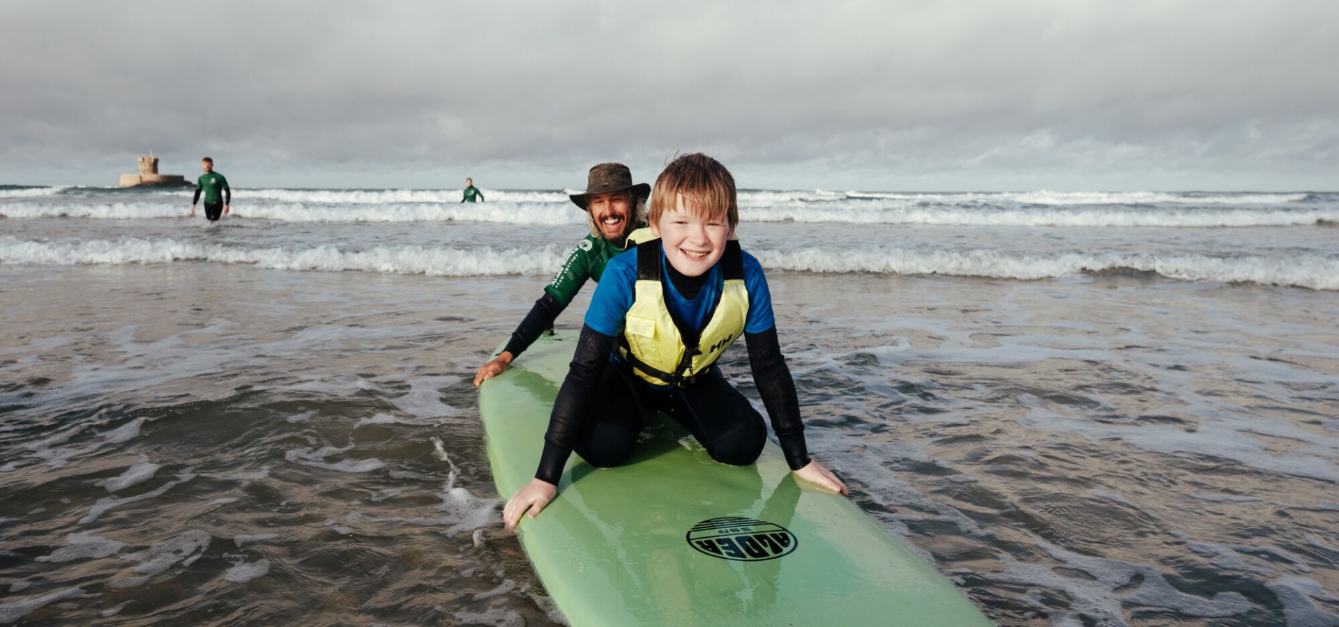 Young boy with additional needs on a surf board, being helped by a coach