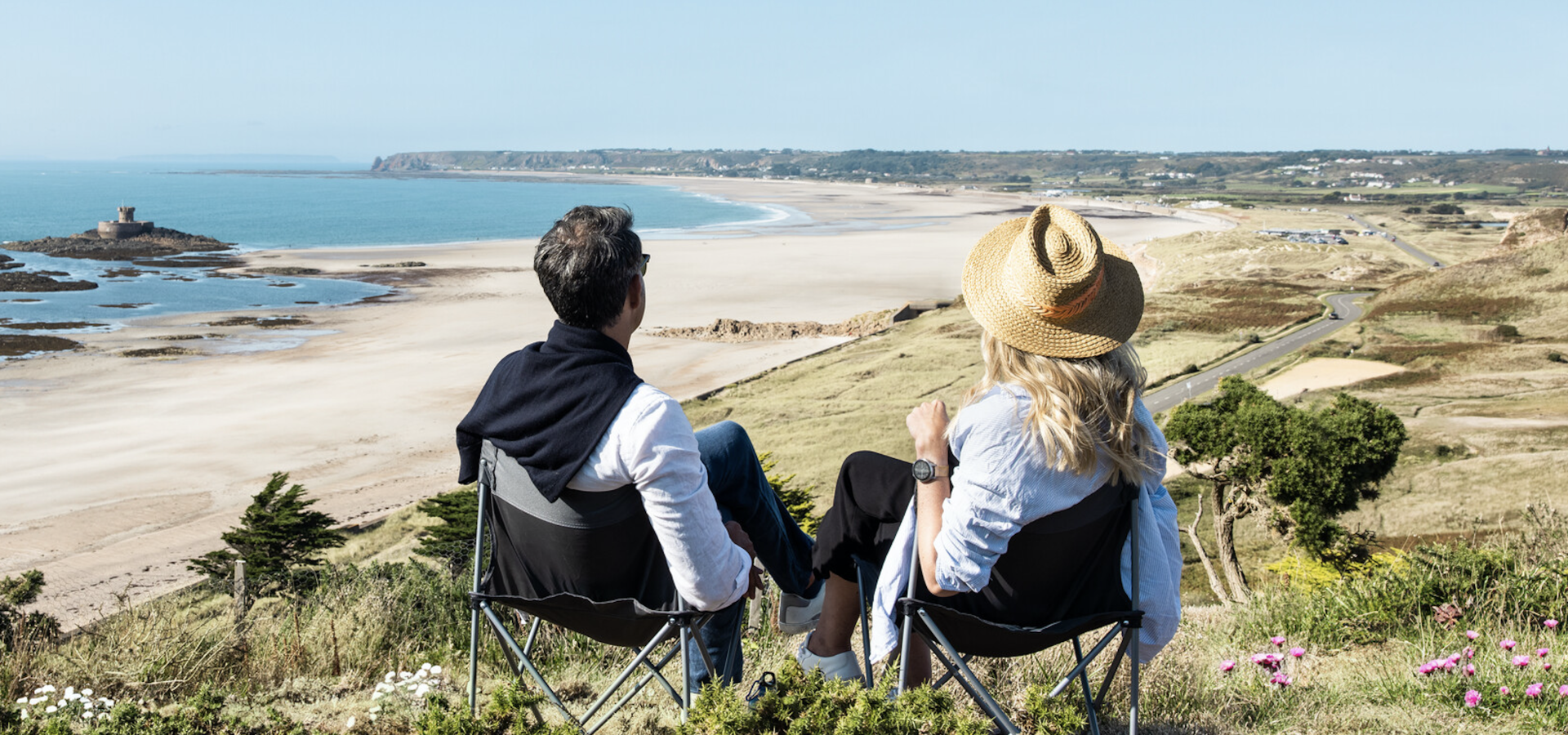 Couple sitting in chairs on a headland overlooking a long stretch of beach and the sea
