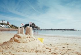 Sand castle on white sandy beach with sea and castle as a back drop
