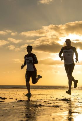 two people running on the beach at sunset