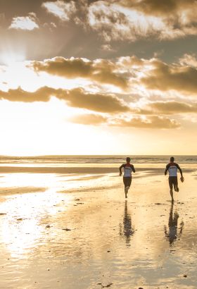 Two people running on the beach towards the sea at sunset