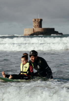 Girl with additional needs on a surfboard with the help of a carer