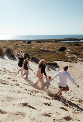 Family running on sand dunes in the sunshine with sea in the background