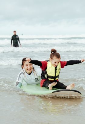 Young girl on a surf board being helped by a Healing Waves surf coach