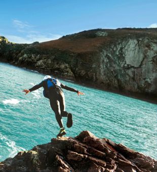 person jumping off a cliff coasteering