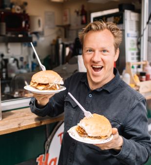 A man at a beach kiosk looking very happy holding two breakfast rolls