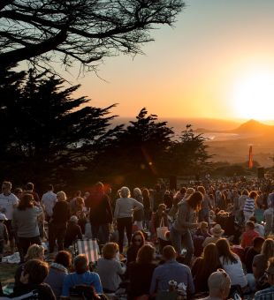 The sun sets over a crowd enjoying a outdoors concert