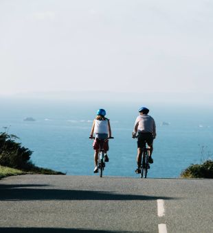 A couple cycling on an empty road with the sea in the background