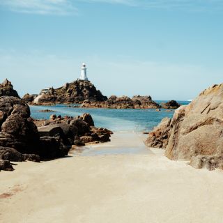 Corbiere lighthouse with sandy causeway and flat calm sea.