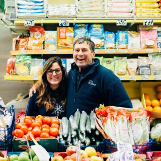 Father and daughter standing in front of a colourful fruit and veg stall