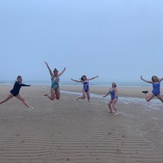 5 girls jumping in the air on the beach.