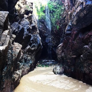 A photo of a mouth opening of a sea cave in Jersey. There is a sandy pathway between two rocks.