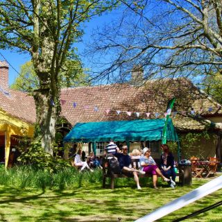 Group of people sitting on benches at La Hogue Bie in the sunshine.