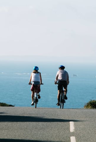 A couple cycling on an empty road with the sea in the background