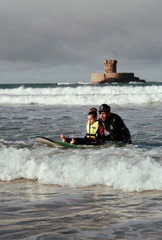 Little girl with additional needs surfing with the help of a carer