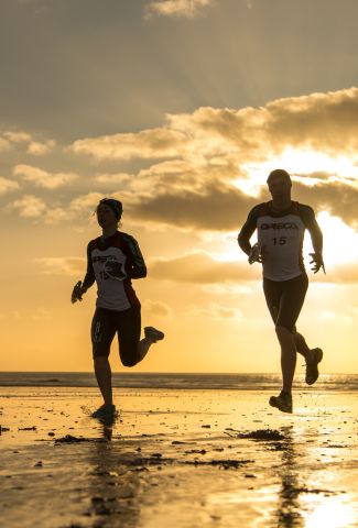 Two athletes running along the beach at sunrise