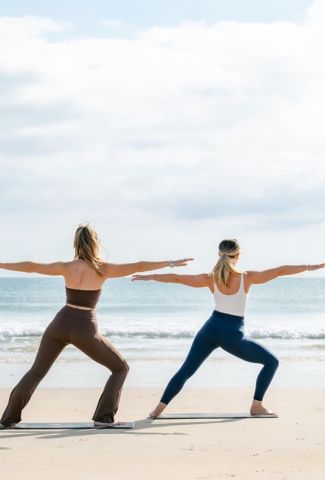 Two people do yoga on a beach