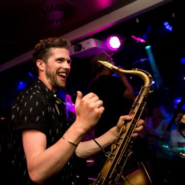 A smiling musician holding a saxaphone in a nightclub.