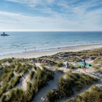 surfers walking through sand dunes towards St. Ouen