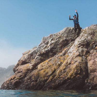 person coasteering and jumping off a cliff into the sea